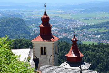 Zvonik cerkev svetega Primoža nad Kamnikom in v ozadju Savska ravan s svojimi mesti.